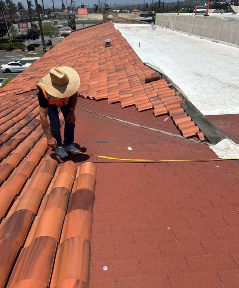 A roofer measuring a tiled roof for replacement holding a tape measure